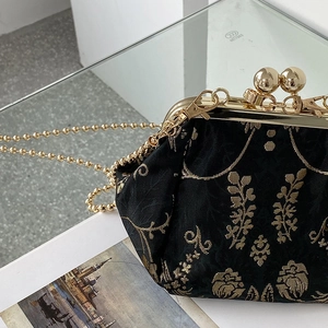 Elegant black floral jacquard kiss-lock bag with gold chain strap in a still life view