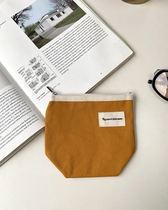 Close-up of mustard yellow canvas mini pouch with zipper on a minimalist book background