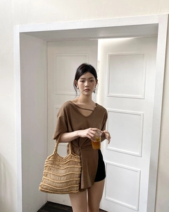 Detail of brown short sleeve top featuring side slit buttons and straw woven tote bag