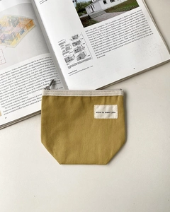 Close-up of mustard yellow canvas pouch showing textured fabric and white woven label