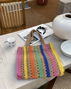 Detail of colorful striped straw tote bag with woven texture on a rustic linen table