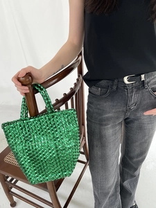 Detail of a bright green woven handbag hanging on a wooden chair in a modern setting