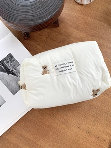 Close-up of quilted cosmetic bag featuring teddy bear embroidery and fabric label details
