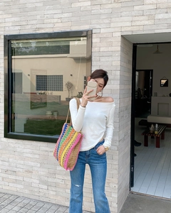 Model wearing a white off-shoulder top and rainbow striped straw tote bag by a wall