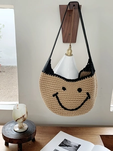 Detail of handmade khaki woven hobo bag featuring a black smiling face and leather strap