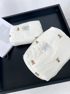 Detail of two white quilted puffer storage bags featuring brown bear embroidery and zippers