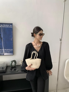 Detail of a beige woven handbag with unique wave texture held by a model in a black top