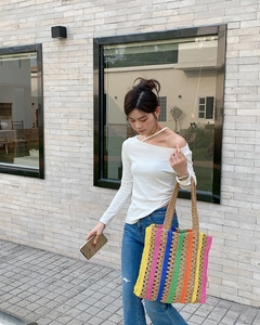 Close-up of a vibrant multi-colored striped crochet tote bag held by a model outdoors