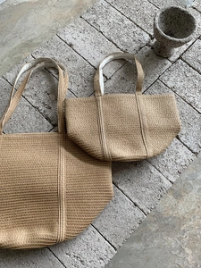 Detail view of woven straw tote bags in two sizes on minimalist stone background