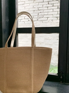 Detailed view of natural straw tote bag with reinforced woven straps on a rustic background