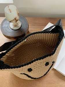 Close-up of woven straw shoulder bag with black smiley face and magnetic metal clasp
