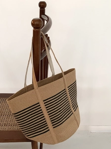 Handmade woven straw tote bag with black horizontal stripes on a dark wooden chair