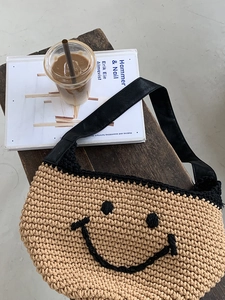 Detail of woven straw shoulder bag with black smiley face and leather strap at a cafe table