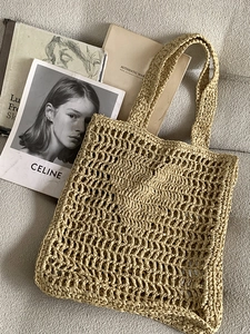 Détail d'un grand sac cabas en paille beige ajouré posé sur un canapé en tissu gris