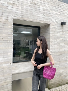 Close-up of bright pink woven basket bag carried by a model against a brick wall