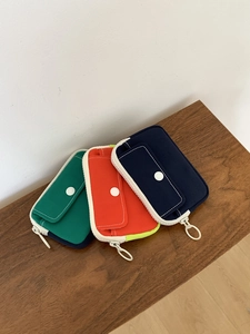 Three colorful canvas mini storage pouches with ring zippers and snap pockets on a wooden bench