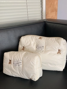 Set of two quilted cream makeup bags with cute bear embroidery on a black sofa