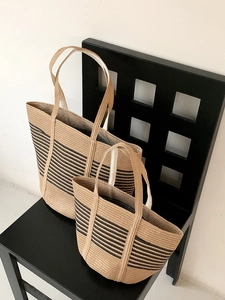 Detail of two woven straw tote bags with black stripes on a stylish black checkered chair