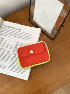 Close-up of the orange mini pouch with yellow trim and white snap button on a book