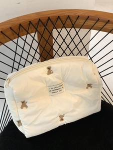 Detailed view of the bear embroidery and quote patch on the white quilted vanity bag
