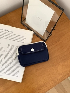 Detail of dark blue canvas mini pouch with snap button and zipper on wooden desk