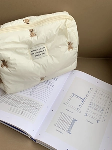 Quilted cream cosmetic bag with cute bear embroidery on a textured background