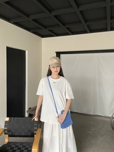 Close-up of blue knitted hollow-out crossbody bag paired with white logo tee and NY cap