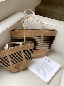 Detail of woven straw tote bag set with black stripes on a white leather sofa