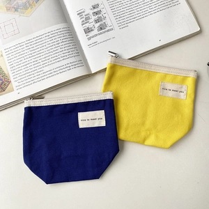 Minimalist canvas makeup pouches in navy and yellow with silver zippers on a desk