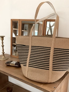 Detail of a large woven straw tote bag with black stripes on a vintage wooden table