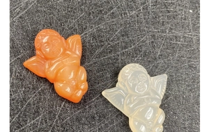 Macro detail of hand-carved agate angel pendants in orange and translucent white