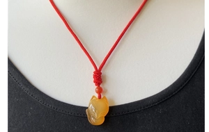 Primo piano del ciondolo a forma di volpe in agata arancione con cordino rosso intrecciato