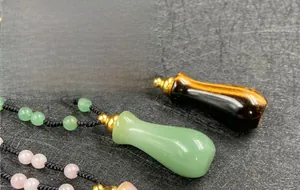 Vista macro di collana intrecciata con ciondoli a forma di boccetta di profumo in pietra