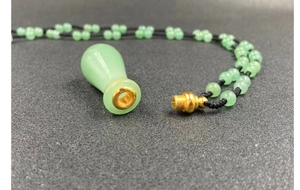Dettaglio del ciondolo porta profumo in giada verde con tappo dorato e catena di perline