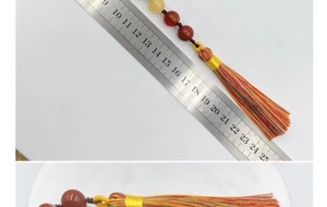 Détail du pompon coloré et de la perle brun-rouge sur le charme avec mesure à la règle