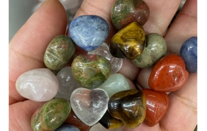 Close-up of mixed natural crystal hearts and stones held in hand for size visualization