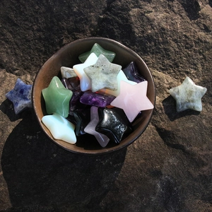 Assorted 30mm star-shaped natural crystal stones in a brown ceramic bowl on dark rock