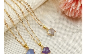 Detailed close-up of three gold star crystal necklaces on textured white fabric