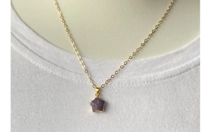 Close-up of a gold star pendant with purple crystal stone worn on a white neck