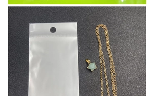 Close-up of gold chain necklace with a light green star-shaped stone pendant in packaging