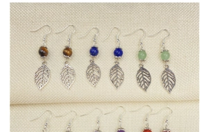 Detail of stone bead earrings featuring silver leaf pendants on a woven fabric background