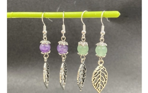 Detail of silver leaf earrings with purple and green beads on a minimalist display