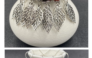 Close-up of silver-tone hollow leaf pendants with intricate veins on white ceramic stand
