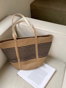 Detail of hand-woven straw tote bag with black stripes on white leather sofa