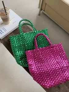 Woven basket tote bag in green and pink metallic finish displayed on a bench