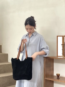 Close-up of black hollow woven tote bag with brown leather handles and metal rivets
