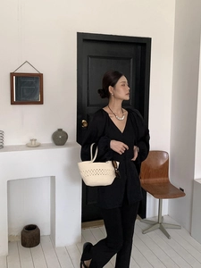 Close-up of a cream woven cotton rope tote bag held by a model in a minimalist black outfit
