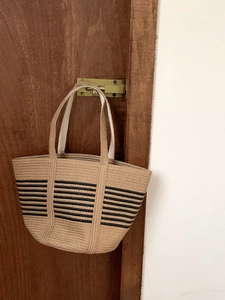 Detail of hand-woven straw tote bag with black horizontal stripes on a wooden door hook