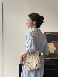 Minimalist cream hand-woven hollow knit shoulder bag worn by a model in a modern room