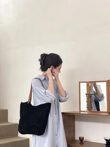 Detail of a black woven tote bag with brown leather straps worn with a blue shirt dress